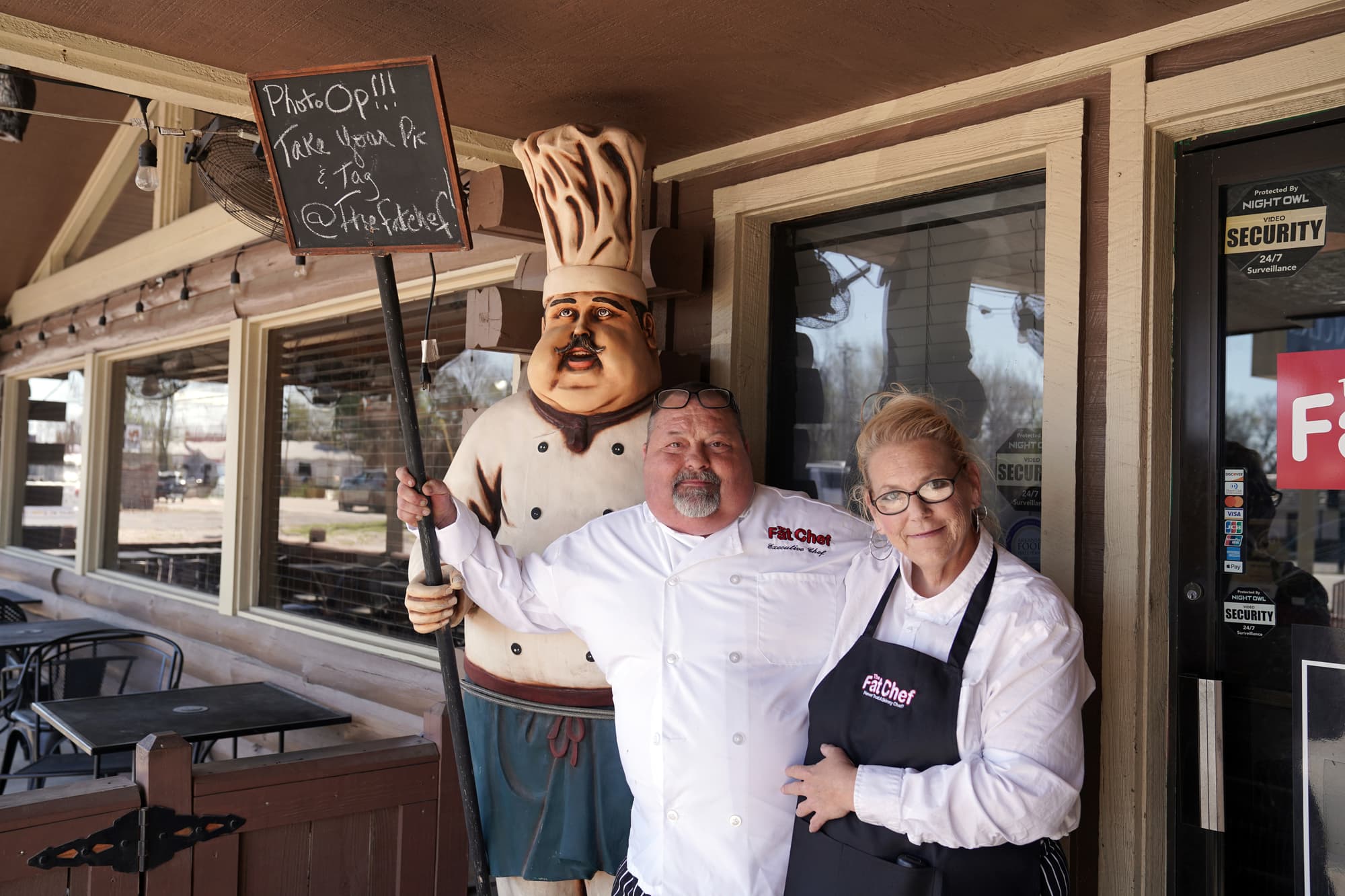 The owners of The Fat Chef standing outdoors next to the chef statue